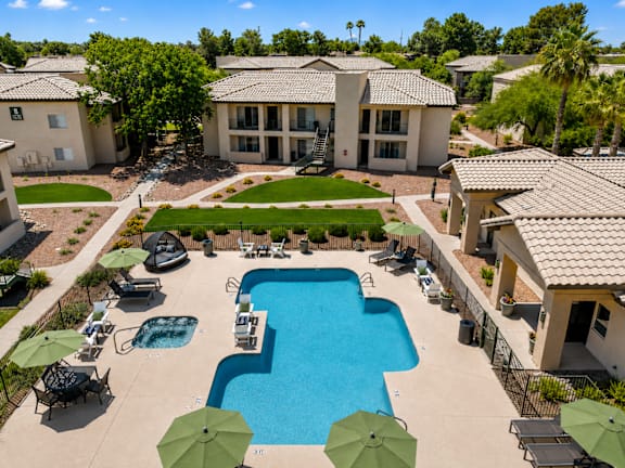A large swimming pool surrounded by lounge chairs and umbrellas in a residential area.