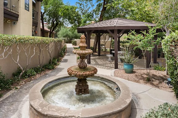 A fountain in the middle of a courtyard with a gazebo in the background.
