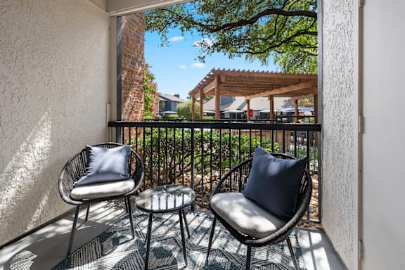 Two chairs and a table are on a balcony.