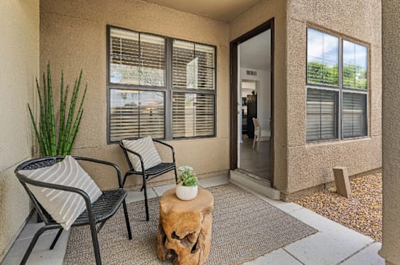 A patio with a table, two chairs and a potted plant.