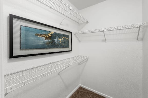 A painting of a landmass surrounded by water hangs on a white wall above a white shelf.
