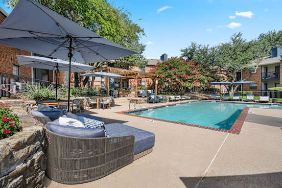 A pool with a hot tub and umbrellas in a backyard.