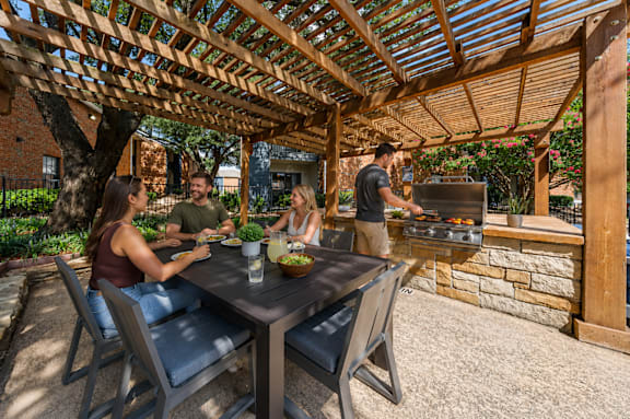 A group of people are sitting at a table under a wooden pergola.
