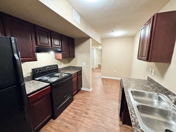 A kitchen with dark wood cabinets and a black refrigerator.