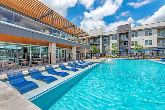 A large swimming pool with blue chairs and a building in the background.