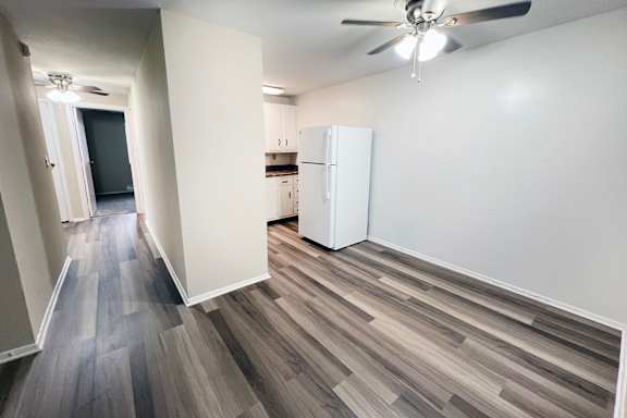 A room with a white fridge and a ceiling fan.