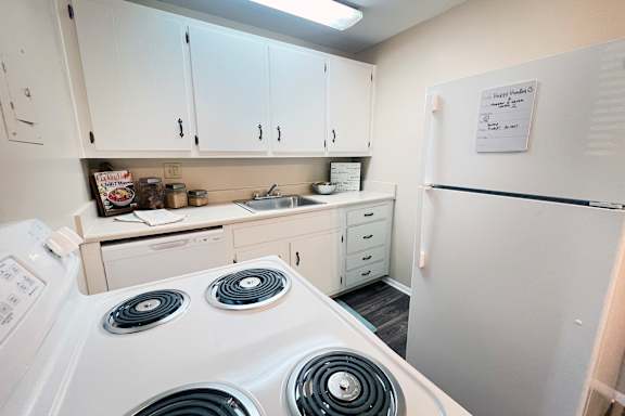 A white stove with two burners is in a kitchen with white cabinets.