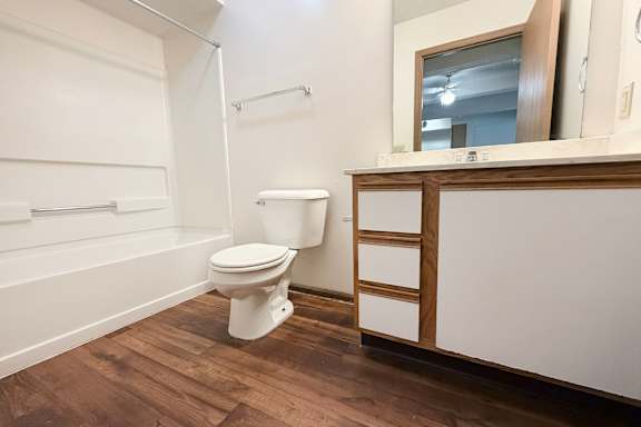 A white toilet sits in a bathroom with wood flooring.