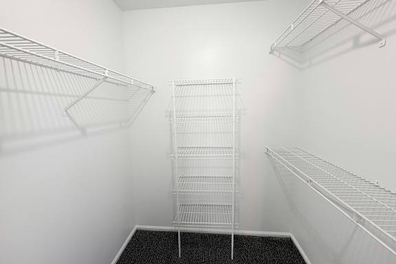 A walk-in closet with white shelving and a black carpeted floor.
