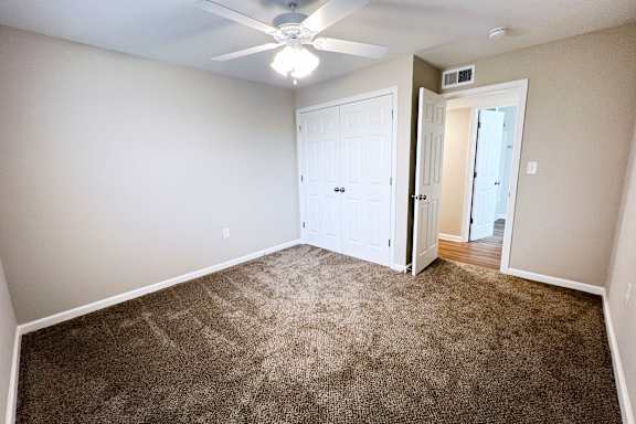 A room with a carpeted floor and a ceiling fan.