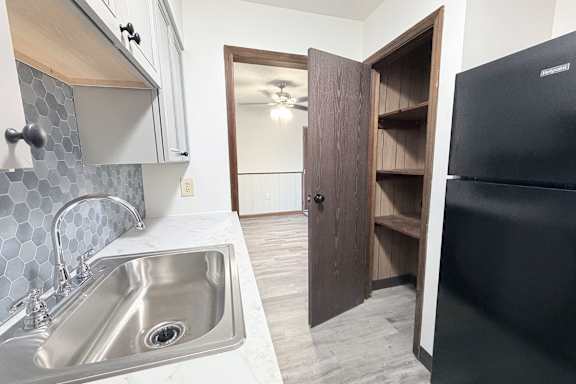 A kitchen with a black refrigerator and a sink with a silver faucet.