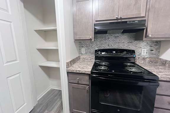 A black stove in a kitchen with white cabinets and a marble countertop.