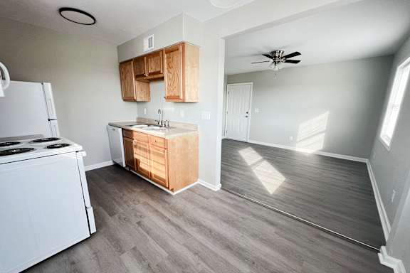 an empty kitchen with white appliances and wood floors