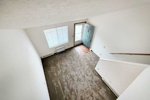 A room with a carpeted floor and a staircase leading to another room.