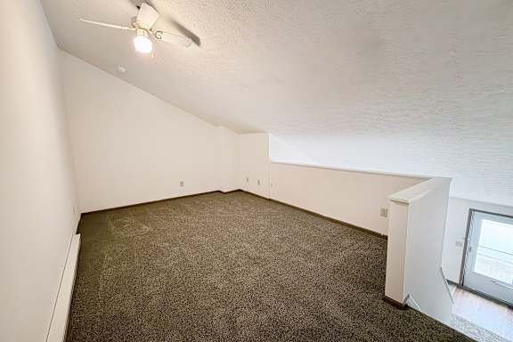 A room with a ceiling fan and carpeted floor.