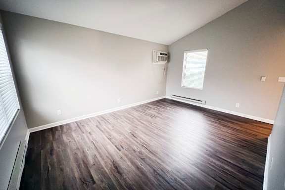 A room with wooden flooring and a window with blinds.