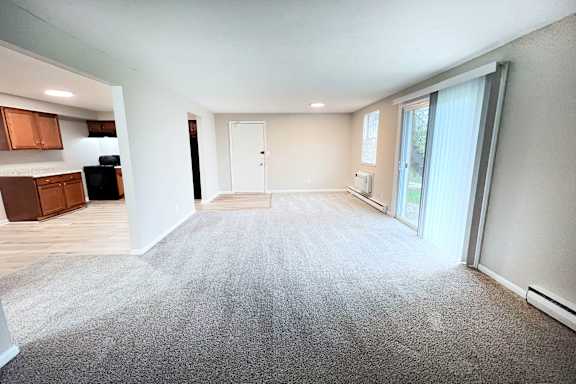 A spacious room with a grey carpet and a sliding glass door.