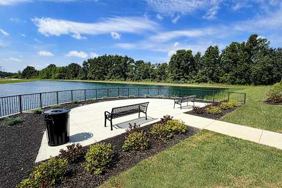 A park with a bench and a trash can near a lake.