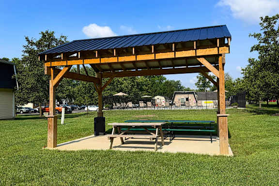 A wooden pavilion with a blue roof is situated in a grassy area.