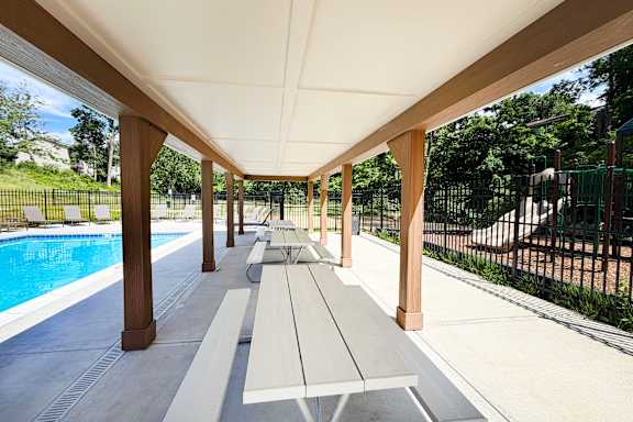 A long covered walkway with benches and a pool in the background.