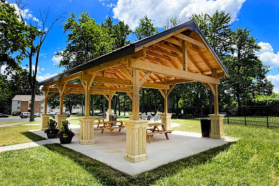 A wooden pavilion with picnic tables is surrounded by green grass.