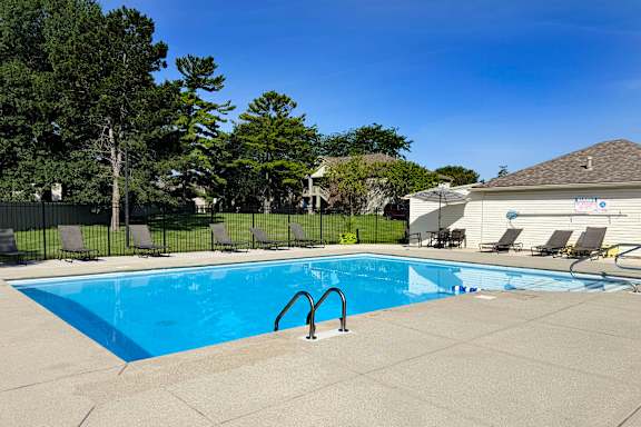 A swimming pool surrounded by a concrete patio and lounge chairs.