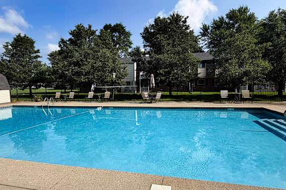 A large swimming pool surrounded by trees and a building in the background.