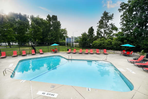 a swimming pool with red lounge chairs and umbrellas  at Hunter's Creek Apartments, Ohio