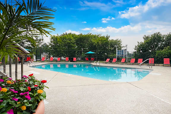 A pool surrounded by red chairs and a green umbrella.