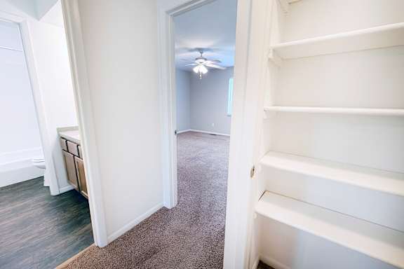 A white shelving unit is in a room with a carpeted floor and a ceiling fan.