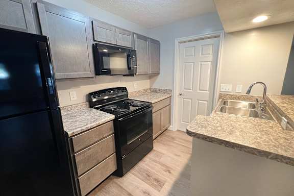 A kitchen with a black refrigerator, a black stove, and a granite countertop.