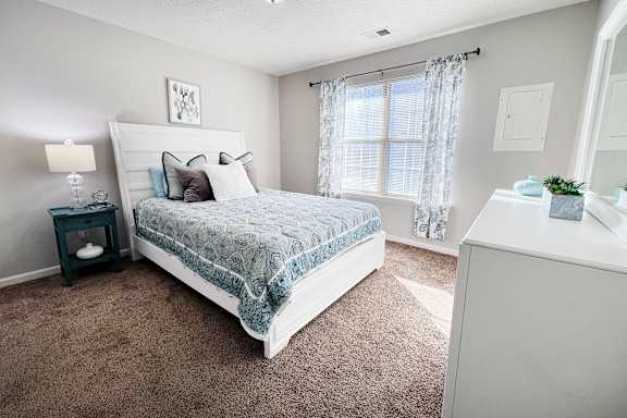 A bedroom with a large bed and a nightstand with a lamp.