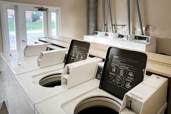 a row of washing machines in a laundromat with two chalkboards on them at Four Worlds Apartments, Ohio, 45231