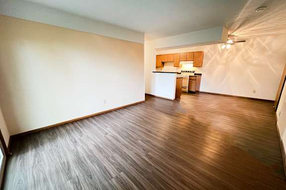 an empty living room with wood floors and a kitchen