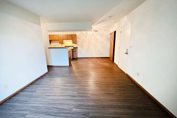 an empty living room with wood flooring and a kitchen