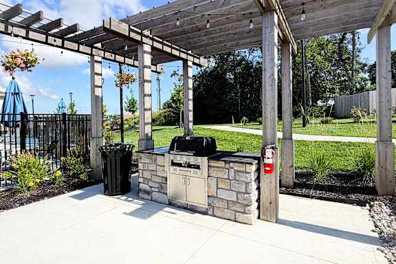 A wooden pergola with a grill and trash cans underneath it.