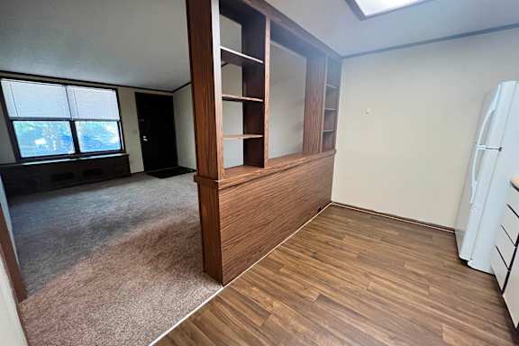 A room with a brown wooden floor and a white fridge.