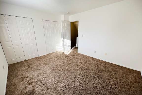 A room with carpeted floor and white walls with a doorway leading to another room.