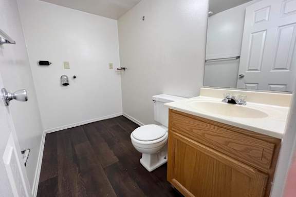 A white toilet sits in a bathroom with wood flooring and a wooden vanity.