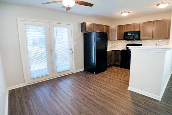 A kitchen with a black fridge and a ceiling fan.