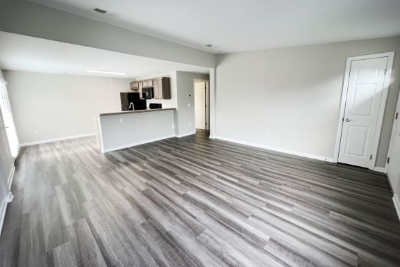 an empty living room with a kitchen in the background