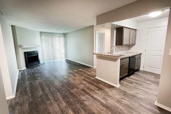 an empty living room with a kitchen and a fireplace