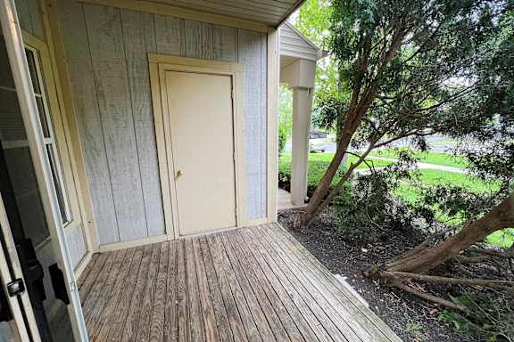 A wooden deck with a white door and a tree in the background.