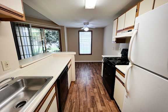 A kitchen with a white fridge, black dishwasher and wooden floors.