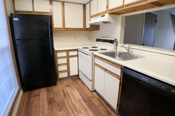 A black refrigerator stands in a kitchen with wooden floors and white appliances.