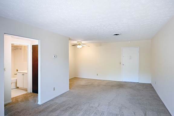 A spacious room with a carpeted floor and a ceiling fan.