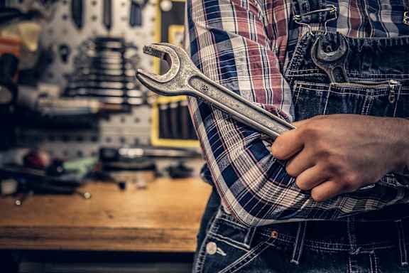 A person in a plaid shirt and jeans holds a wrench in their hand.