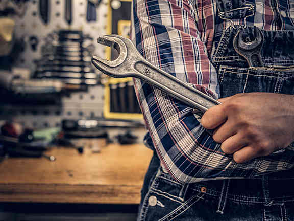 A person in a plaid shirt and jeans holds a wrench in their hand.