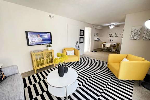 A living room with a television, yellow chairs, and a black and white striped rug.