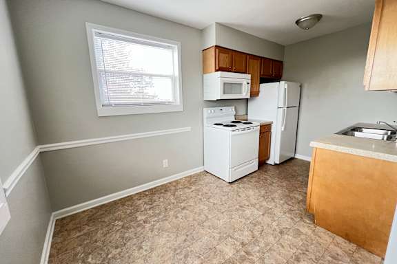 an empty kitchen with white appliances and a window